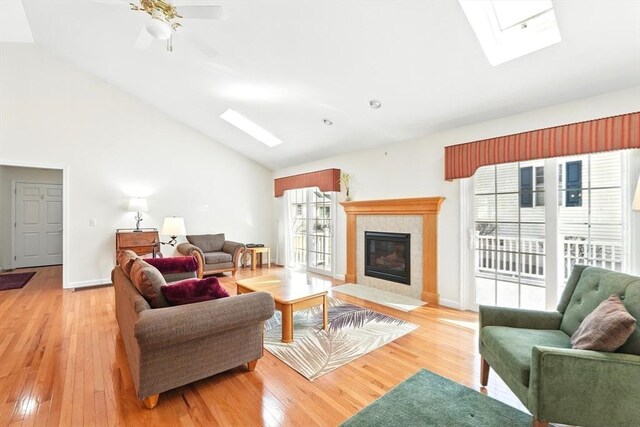 living area with a fireplace, a skylight, light wood-style floors, and baseboards