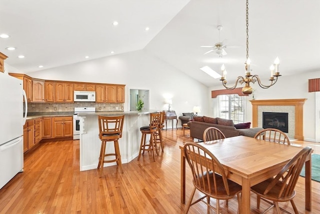 dining room with light wood-type flooring, a glass covered fireplace, recessed lighting, a notable chandelier, and high vaulted ceiling