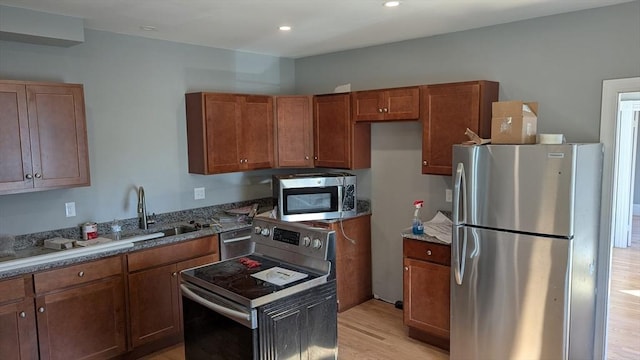 kitchen featuring stainless steel appliances, light wood-type flooring, brown cabinetry, and a sink