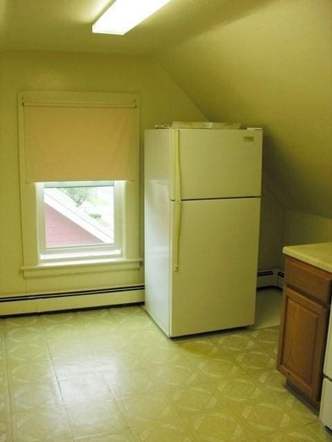 kitchen featuring light floors, lofted ceiling, a baseboard radiator, brown cabinetry, and freestanding refrigerator