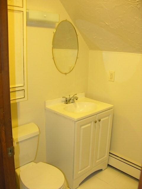 half bathroom with a baseboard heating unit, toilet, lofted ceiling, and vanity