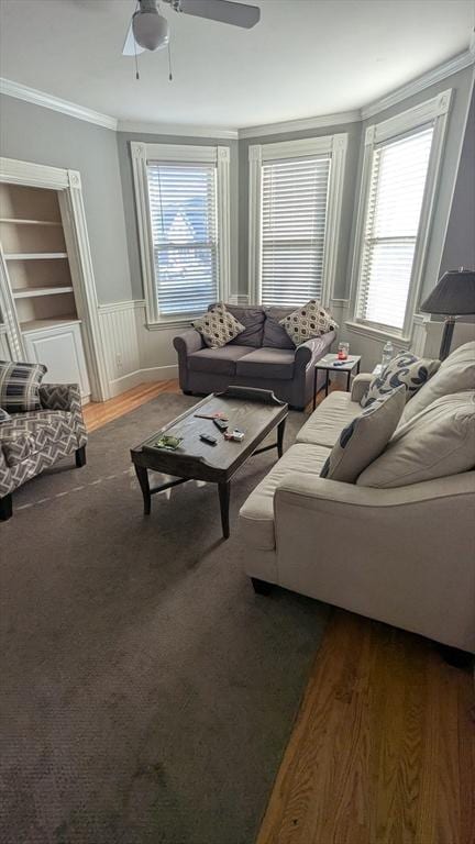 living room featuring a ceiling fan, wainscoting, crown molding, and wood finished floors