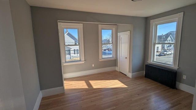 unfurnished bedroom with radiator heating unit, baseboards, and wood finished floors