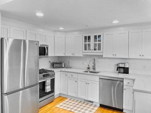 kitchen with white cabinets, glass insert cabinets, stainless steel appliances, light wood-type flooring, and a sink