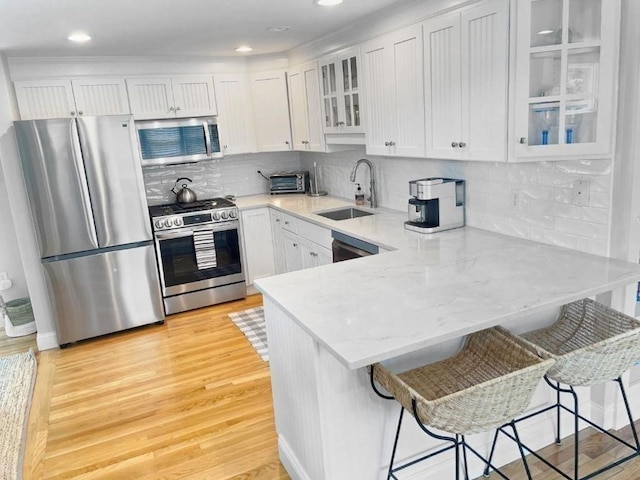 kitchen with a sink, white cabinets, appliances with stainless steel finishes, a kitchen bar, and glass insert cabinets