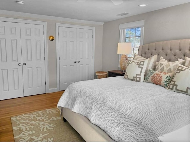 bedroom featuring ceiling fan, wood finished floors, visible vents, baseboards, and multiple closets