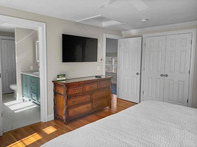 bedroom featuring light wood finished floors, attic access, a ceiling fan, ensuite bath, and a closet