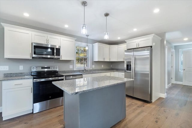 kitchen with appliances with stainless steel finishes, white cabinets, a sink, and light wood finished floors