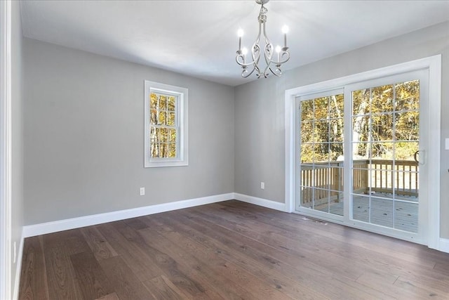 unfurnished room featuring an inviting chandelier, baseboards, and dark wood finished floors