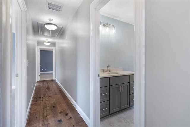 hallway with visible vents, attic access, a sink, wood finished floors, and baseboards