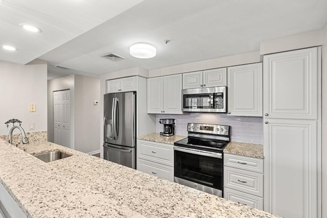 kitchen featuring light stone counters, visible vents, a sink, decorative backsplash, and appliances with stainless steel finishes