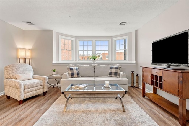 living room featuring baseboards, wood finished floors, visible vents, and a textured ceiling