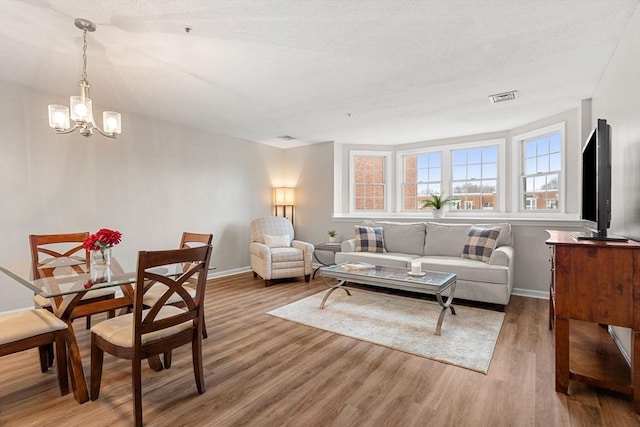 living area featuring visible vents, baseboards, a notable chandelier, and wood finished floors