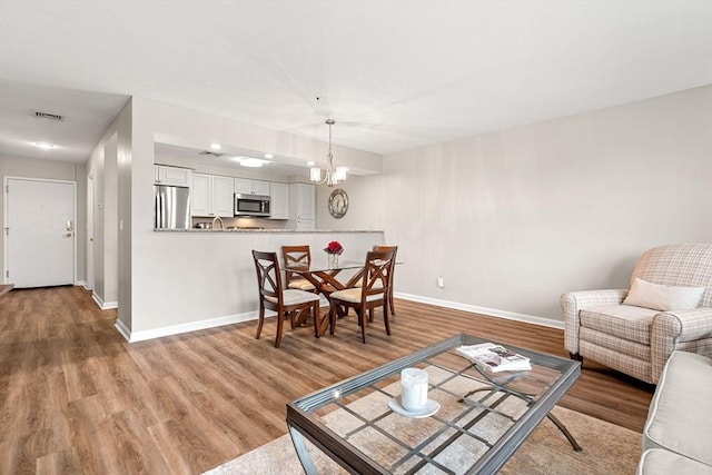 living room with visible vents, an inviting chandelier, baseboards, and wood finished floors