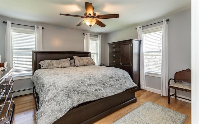 bedroom with light wood-type flooring, ceiling fan, a baseboard heating unit, and multiple windows
