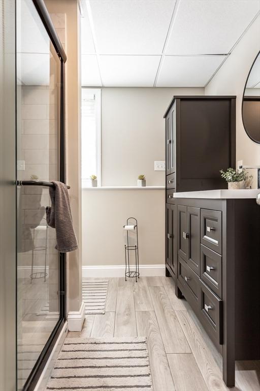 full bathroom with vanity, wood finished floors, baseboards, a drop ceiling, and a shower stall