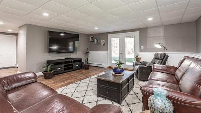 living room with french doors, light wood-type flooring, a wainscoted wall, a baseboard radiator, and a drop ceiling