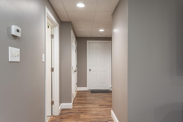 hall with recessed lighting, baseboards, a drop ceiling, and wood finished floors
