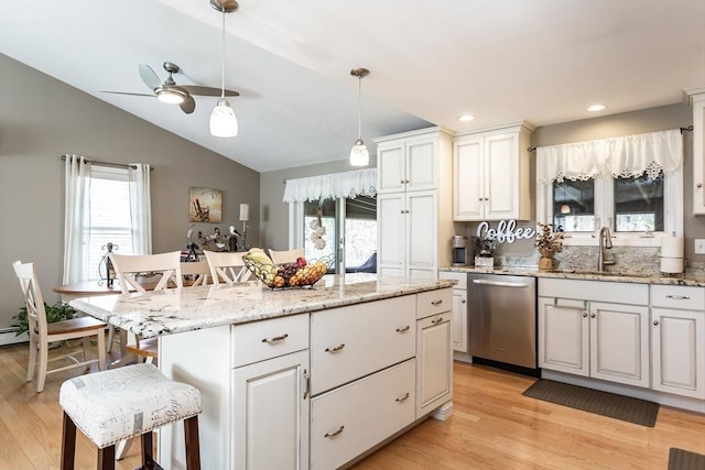 kitchen featuring ceiling fan, a sink, a kitchen breakfast bar, light wood-style flooring, and stainless steel dishwasher