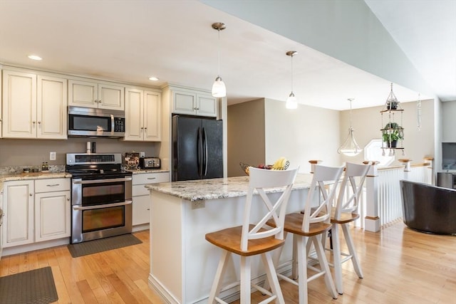 kitchen featuring light stone countertops, a kitchen breakfast bar, light wood-style flooring, appliances with stainless steel finishes, and hanging light fixtures