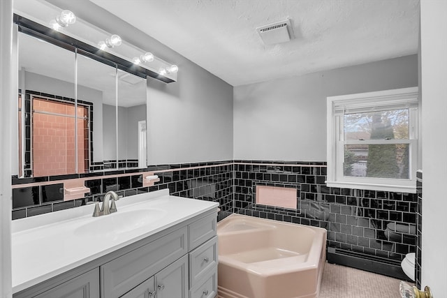 bathroom featuring vanity, a textured ceiling, a washtub, and tile walls