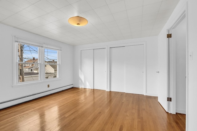 unfurnished bedroom with a baseboard heating unit, two closets, and hardwood / wood-style floors