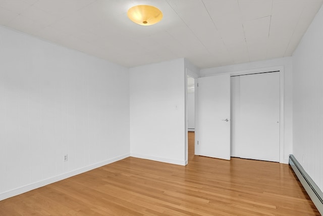 unfurnished bedroom with a closet, a baseboard radiator, and light wood-type flooring