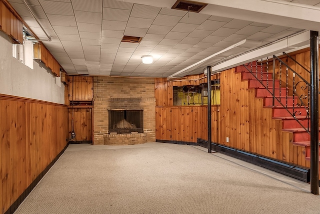 basement featuring wood walls, light carpet, and a brick fireplace