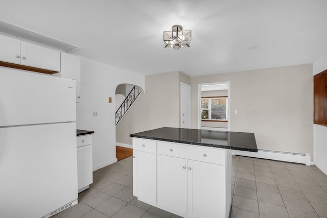 kitchen featuring light tile patterned flooring, a kitchen island, baseboard heating, white cabinets, and white fridge