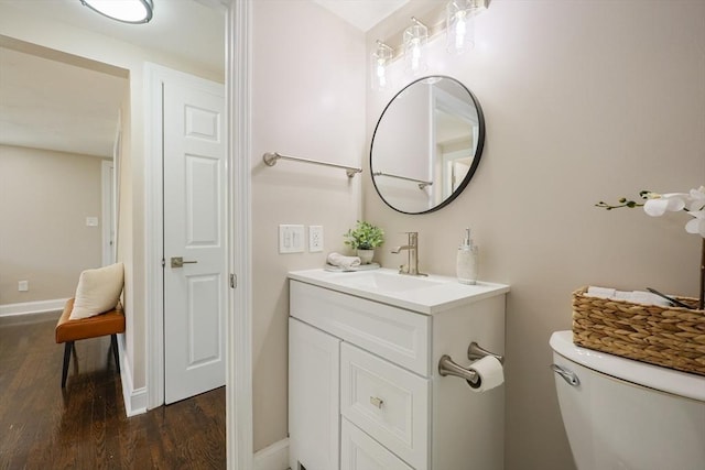 half bathroom featuring wood finished floors, vanity, toilet, and baseboards