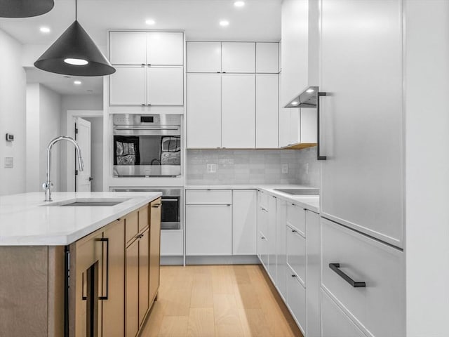 kitchen with a sink, double oven, light countertops, recessed lighting, and white cabinetry