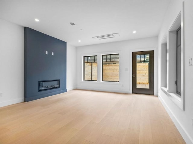 spare room featuring light wood-style floors, a large fireplace, recessed lighting, and baseboards