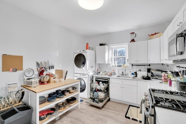 kitchen with stacked washing maching and dryer, appliances with stainless steel finishes, white cabinets, and light wood-type flooring