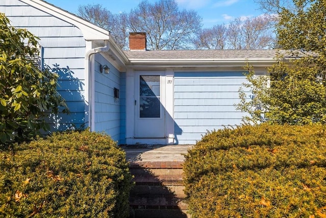 entrance to property featuring a shingled roof and a chimney