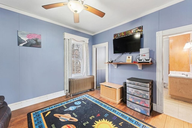 sitting room with radiator, baseboards, ornamental molding, wood finished floors, and a ceiling fan