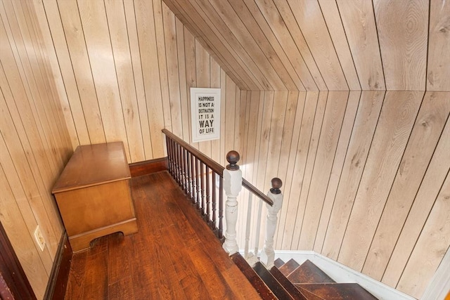 stairs with vaulted ceiling, wood finished floors, and wood walls