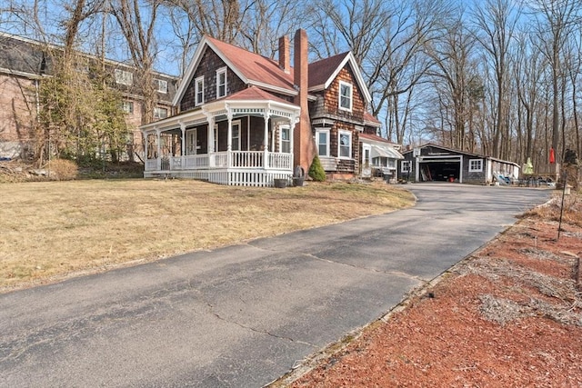 view of front of property with a front yard, driveway, a porch, a chimney, and an outdoor structure