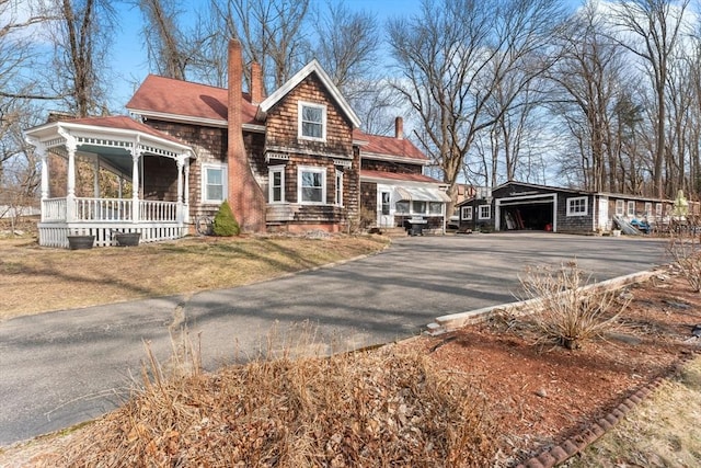 view of front facade featuring driveway, a porch, a chimney, an outdoor structure, and a garage