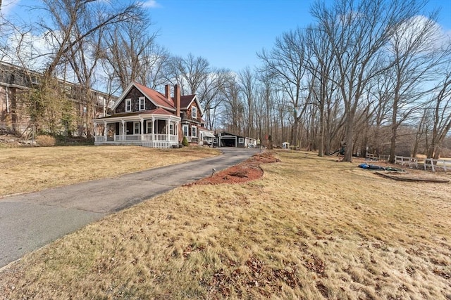 view of front of home featuring a porch, a front yard, a chimney, a carport, and driveway