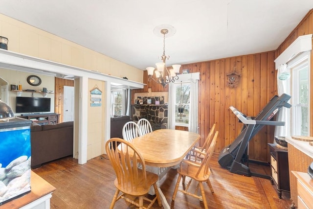 dining space with a notable chandelier, wood finished floors, wood walls, and a wealth of natural light