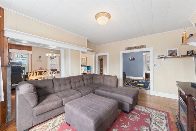 living room featuring a notable chandelier, ornamental molding, baseboards, and wood finished floors