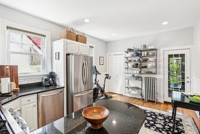 kitchen with light wood-style floors, stainless steel appliances, white cabinets, and radiator heating unit