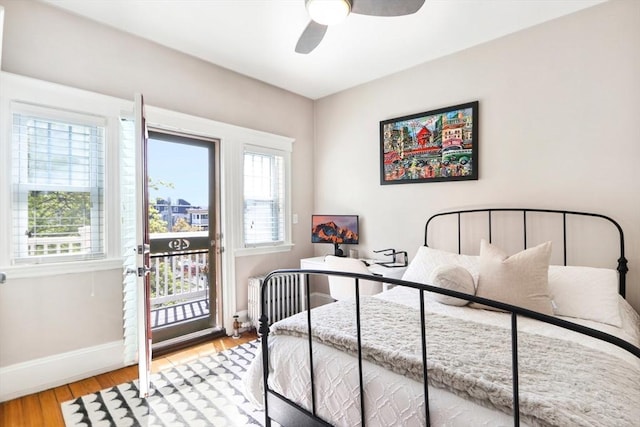 bedroom featuring radiator, wood finished floors, a ceiling fan, baseboards, and access to exterior