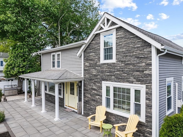1091 Tobey St, New Bedford, MA 02745 - back of property with stone siding, a patio, and roof with shingles