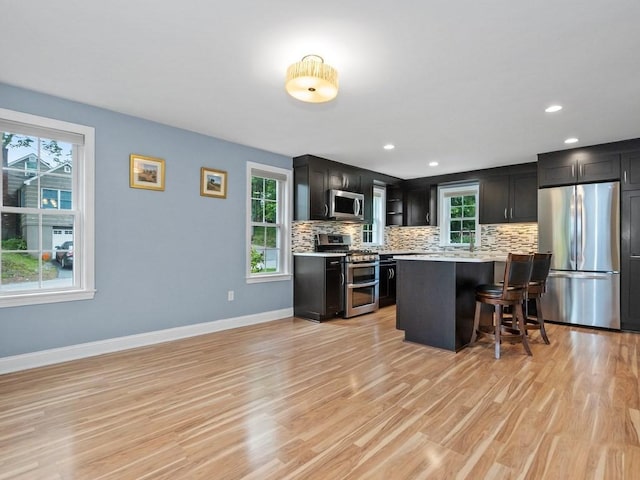 4 University Park, Waltham, MA 02453 - kitchen featuring appliances with stainless steel finishes, a kitchen breakfast bar, light countertops, decorative backsplash, and light wood finished floors