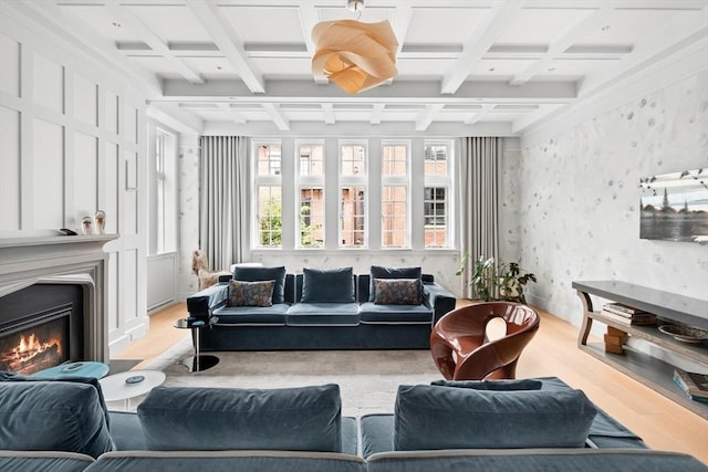 living area featuring wallpapered walls, a glass covered fireplace, light wood-style floors, and coffered ceiling