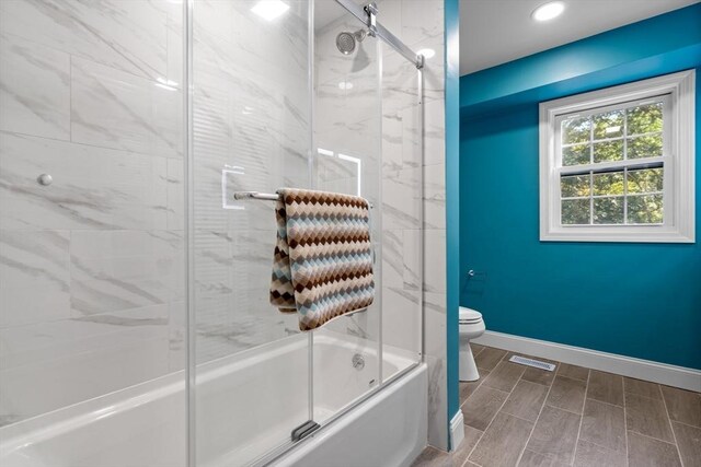 bathroom featuring combined bath / shower with glass door and toilet