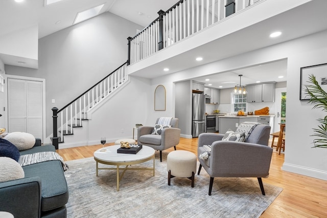 living room featuring light hardwood / wood-style flooring, a skylight, and high vaulted ceiling