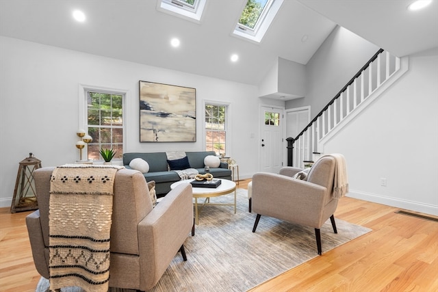 living room with light wood-type flooring, high vaulted ceiling, a skylight, and a wealth of natural light