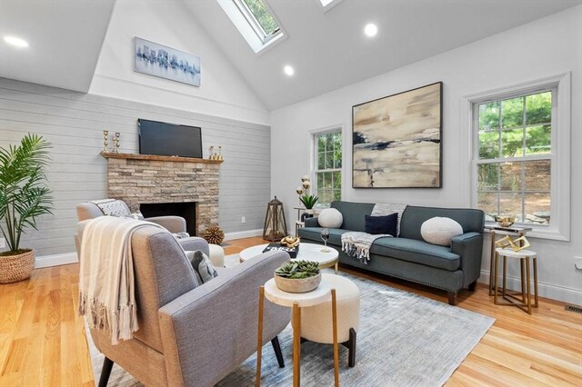 living room with high vaulted ceiling, wood-type flooring, a skylight, and a stone fireplace